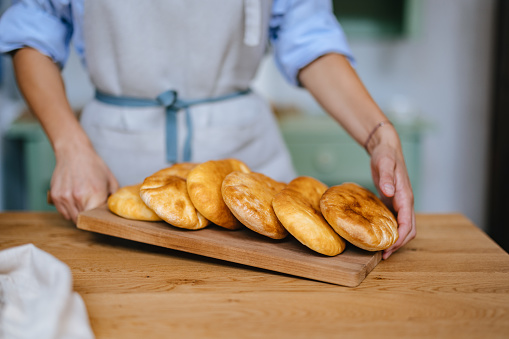 Close up shot of an unrecognizable female baker holding a wooden cutting board with freshly baked bread loaves.