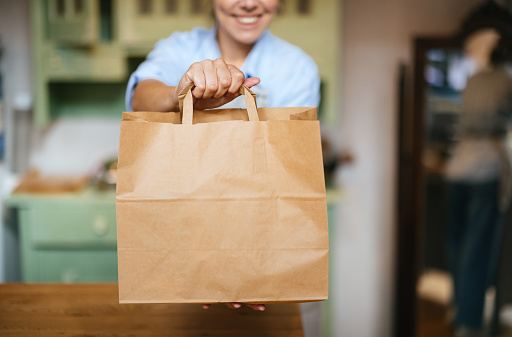 Close up shot of an unrecognizable woman holding a paper bag offering it to an anonymous customer at the store.