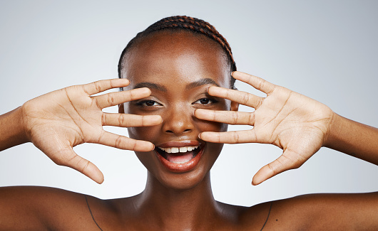 Wellness, hands and portrait of black woman for skincare, beauty reveal and excited on a studio background. Smile, young and African person with a gesture for clean facial skin or a dermatology glow