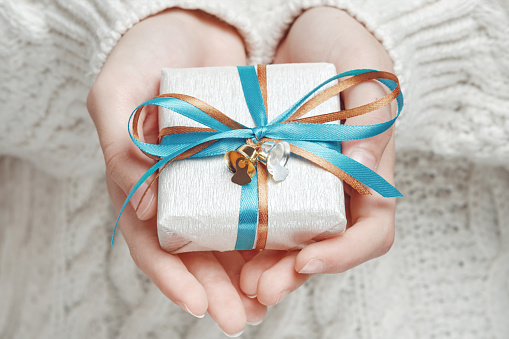 Female hands hold a beautifully wrapped gift with a bow and bells. Merry Christmas, Happy New Year, Boxing Day, Birthday.