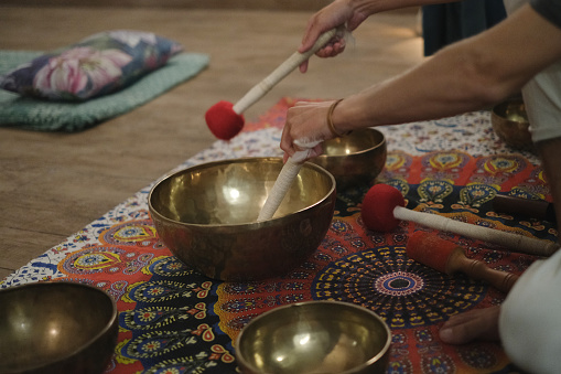 Close-up shot of unrecognizable man playing a Tibetan singing meditation bowl during sound healing yoga class