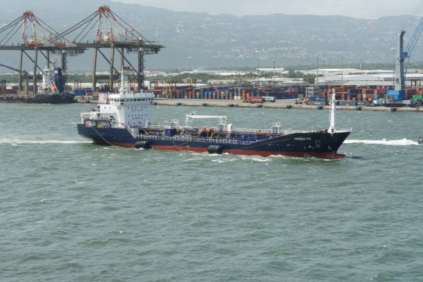 Small oil chemical tanker PANDA PG with blue hull, white superstructure and big rubber fender is leaving port of Kingston. Kingston, Jamaica - 05 25 2023: Small oil chemical tanker PANDA PG with blue hull, white superstructure and big rubber fender is leaving port of Kingston during windy weather. Behind are gantry cranes. kingston harbour stock pictures, royalty-free photos & images