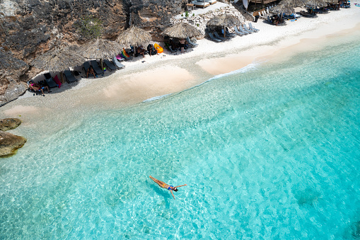 Woman floating in water, palapas and lounge chairs on playa kalki, Curacao