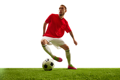Portrait of male football player in red jersey standing with football on pitch during match.