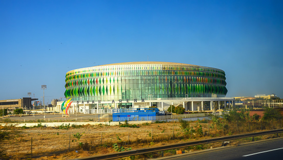 Dakar, Senegal - March 01, 2023 : Exterior view of the impressive Dakar Arena, a modern multi-purpose indoor venue, captured from the road in Diamniadio, near Dakar, Senegal, under a clear sky.