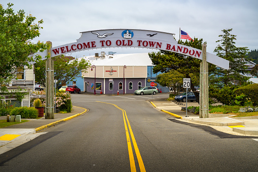 Bandon, Oregon, USA - June 07, 2023 : 'Welcome to Old Town Bandon' street arch sign with the Broken Anchor Bar and Grill in the background, capturing the charming atmosphere of Bandon, Oregon.