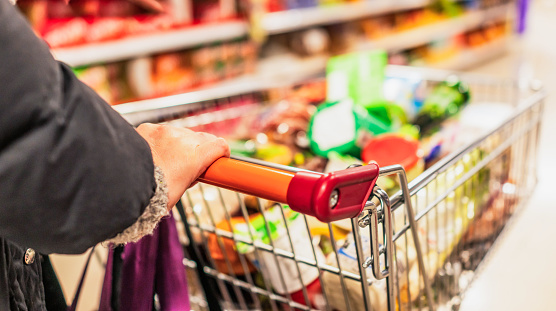 Close up of a woman's hand on a supermarket trolley, filling up with products during a weekly shop.