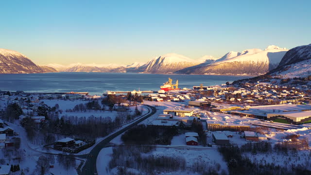 Aerial View of Dramatic Winter Sunset Over Scenic Town by Fjord with Cars Driving on Road in Norway