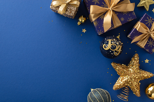 Luminous Santa's Gifts Concept. Overhead shot of glistening blue and gold-wrapped presents, baubles, star decor, sequins on a luxurious blue backdrop with space for your greeting text or advert