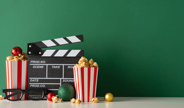 istock Fancy film premiere highlighting delectable snacks. Side view table adorned with film producer's clapper, 3D glasses, popcorn in containers, complemented by ornaments against green wall for movie ads 1765346324