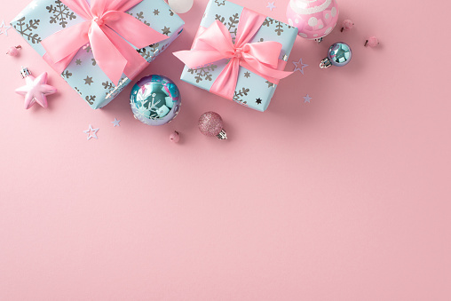 Festive New Year theme. Overhead shot of ornaments, blue gift packages with ribbons, pink mistletoe berries, confetti on soft pastel pink backdrop with room for text or promotion