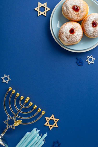 istock Hanukkah-themed vertical top view table setting with sufganiyot, menorah, candles, and the Star of David symbols on a blue background, perfect for your celebration 1765347421