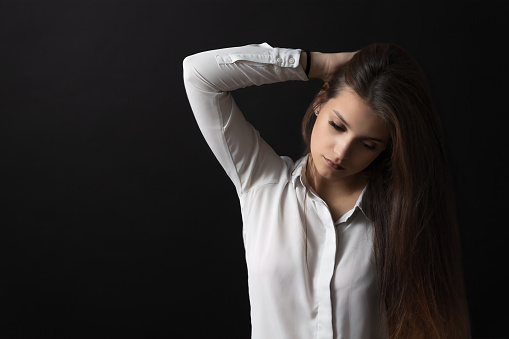 Portrait of sad long haired girl posing in studio on black background.  Horizontally.