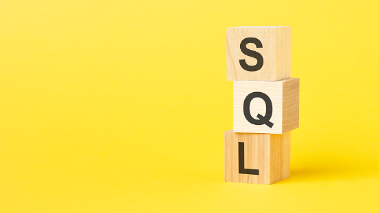 wooden cubes with text sql - short for structured query language. yellow background
