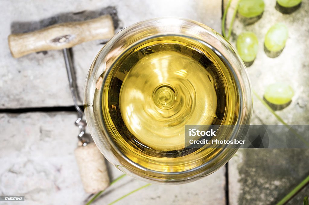 White wine Glass of white wine on top of the background of stone, corkscrew and cork, vine leaves and grapes. Alcohol - Drink Stock Photo