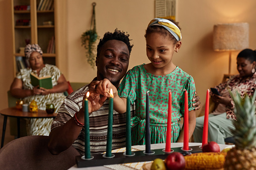 Father helping excited little daughter to light candles for Kwanzaa celebration