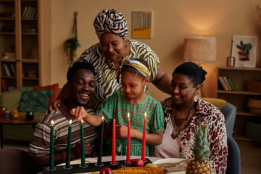 Black three generation family lightning Mishumaa Saba, seven colorful candles for Kwanzaa celebration