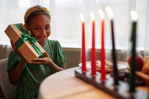 aufgeregtes mädchen, das kwanzaa-geschenk schüttelt - kinara stock-fotos und bilder