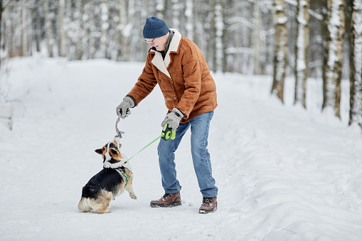 Happy senior man playing with dog in winter park