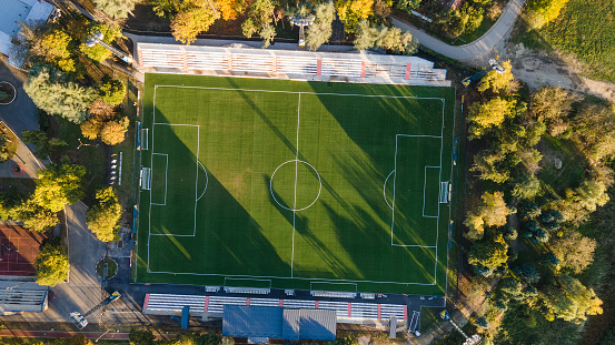 Aerial top down view above the people playing football on a pitch among the forest. Aerial top view of soccer football sport recreation field ground.