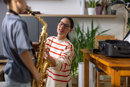 Young boy musician practicing playing saxophone with his female teacher at home.