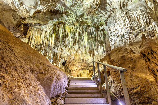 Staircase for visitors in Prometheus Cave Natural Monument in Georgia with stalactites and stalagmites on the ceiling, colorful illuminated rock formations.
