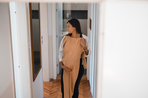 Happy pregnant woman looking herself in a mirror when trying on maternity dress