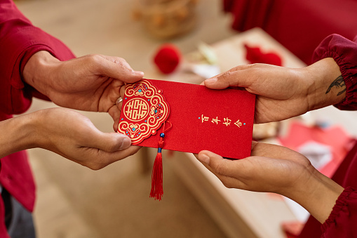 Close up of two people handing ornate red envelope as Chinese New Year tradition for good luck Translation Have overflowing abundance hundred years
