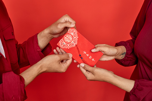 Close up of couple giving red hongbao envelope with good luck inscription as present for Chinese New year, copy space Translation Have overflowing abundance hundred years