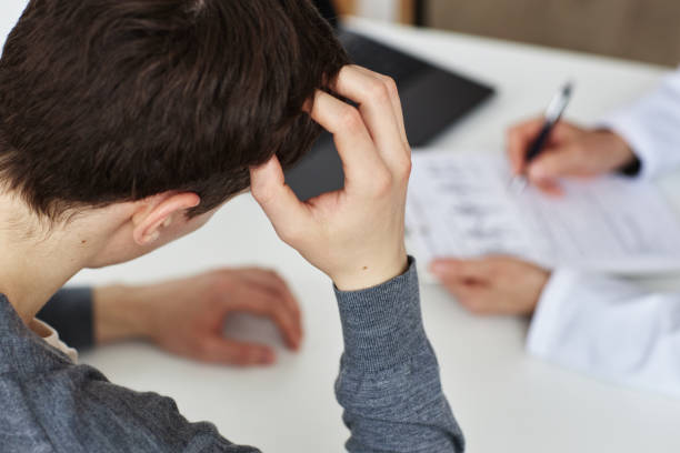 homme troublé à angle élevé se grattant la tête pendant la consultation avec le médecin - human scalp photos et images de collection