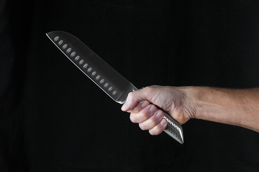 Chef kitchen knife santoku in hand  close up on a black background