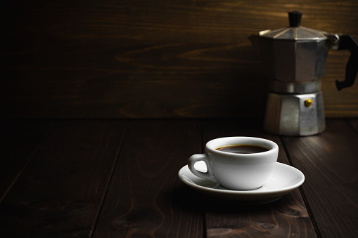 White cup of coffee with old metal coffee percolator on dark wooden background