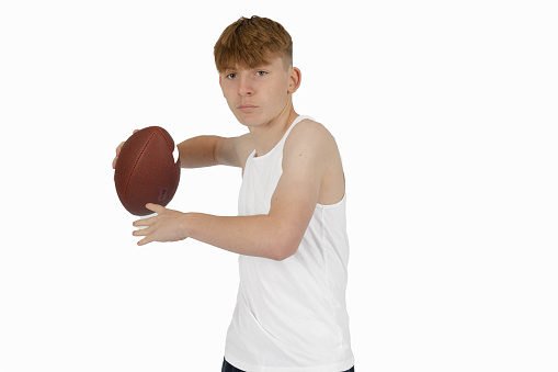 Caucasian teenage boy in a white sleeveless vest about to throw an American Football