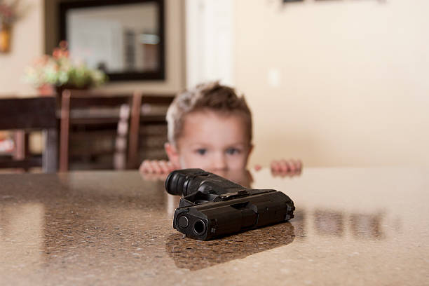 A small child staring at a hand gun within reach on a table Little boy at kitchen counter and a parent has left thier gun on the counter top unattended and he is curious about the gun. gun control photos stock pictures, royalty-free photos & images