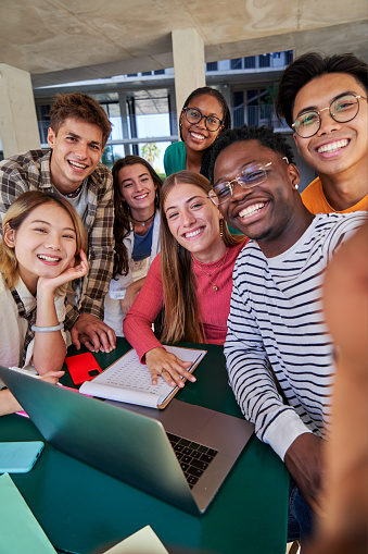 Vertical photo of a group of multiracial students taking a selfie while gathering to study together at campus university. Copy space.