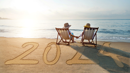 Couple sitting on deck chair at beach with new year number 2024