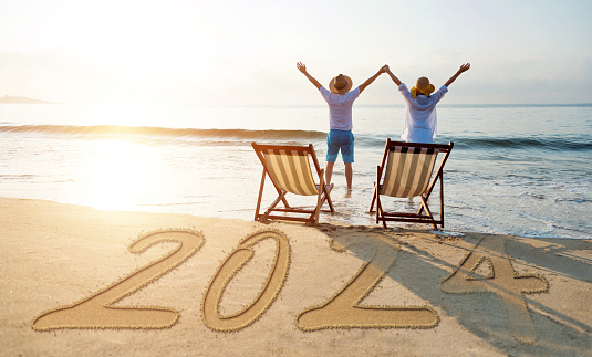 Couple standing on new year number 2024 beach with arms raised