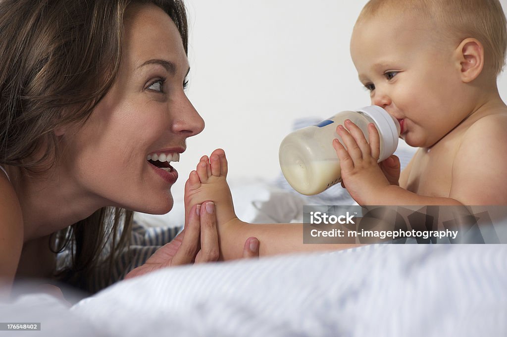 Bebê a beber da garrafa com sua mãe sorridente - Foto de stock de Bebê royalty-free