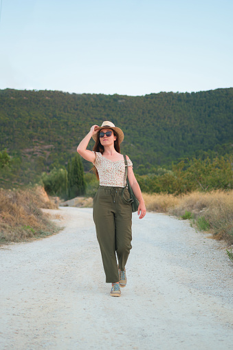 Portrait of a woman walking in the countryside wearing a straw hat and sunglasses