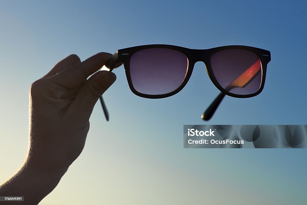 Backlit Hand and Sunglasses 01 Hand Holding Black Sunglasses at sunset in front of vibrant blue sky. The Sun iluminates de scene with the golden light of dawning.  Backlit Adolescence Stock Photo