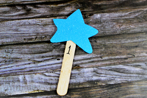 A yellow star fixed to a wooden tongue depressor with number 1 as a reward for school child, glittered colorful Eva foam sheets, colored cardboard, rubber pad, sponge papers for school arts and crafts, selective focus