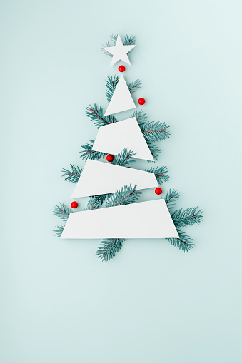 Creative minimalistic Christmas tree mockup with blue Christmas tree branches and red berries on blue pastel background.