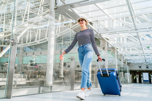 Young cheerful woman walking with her luggage at the airport