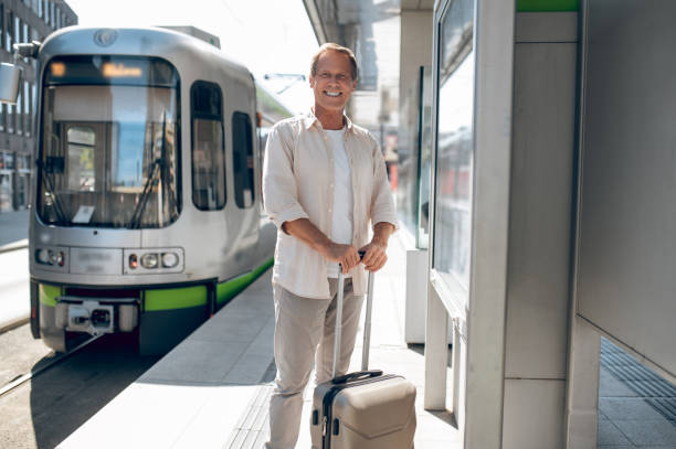 istock Man at train station standing at railroad station platform with suitcase. 1765582408