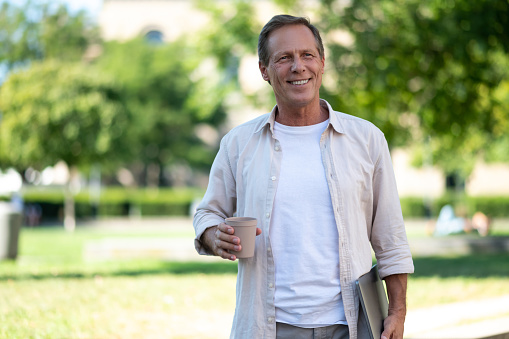 Smiling handsome man holding laptop in city park.