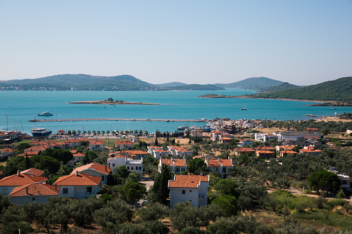 A panoramic view of Cunda Island, showcasing the vibrant turquoise sea, local architecture, boats, and surrounding hills.