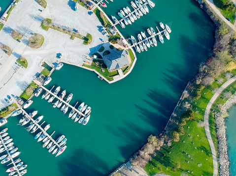 Aerial view of sailing yachts and boats near wooden piers. Top view of American city large boat parking near sea coast. Island and parks with green grass. Beginning of summer concept.