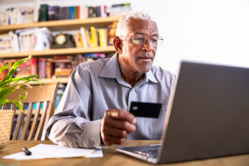 A senior black man shopping online using a credit card an a laptop