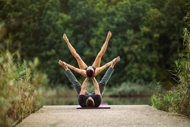 Young man and woman doing acroyoga by lake Young man and woman doing acroyoga pose by lake, strength, trust, perfect synchronization, balance and harmony, forest in the background acroyoga stock pictures, royalty-free photos & images