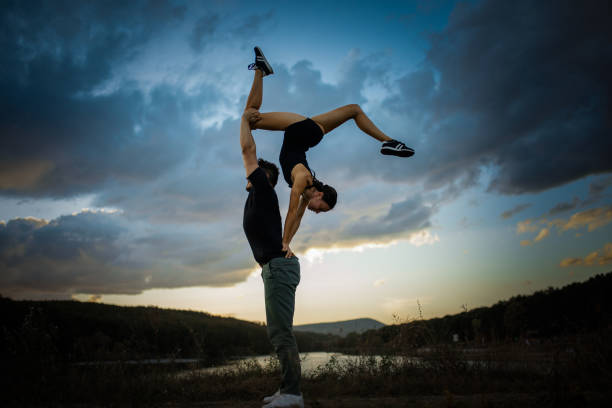 Young man and woman doing acroyoga pose, strength, trust, perfect synchronization, balance and harmony, in dusk, blue sky in the background